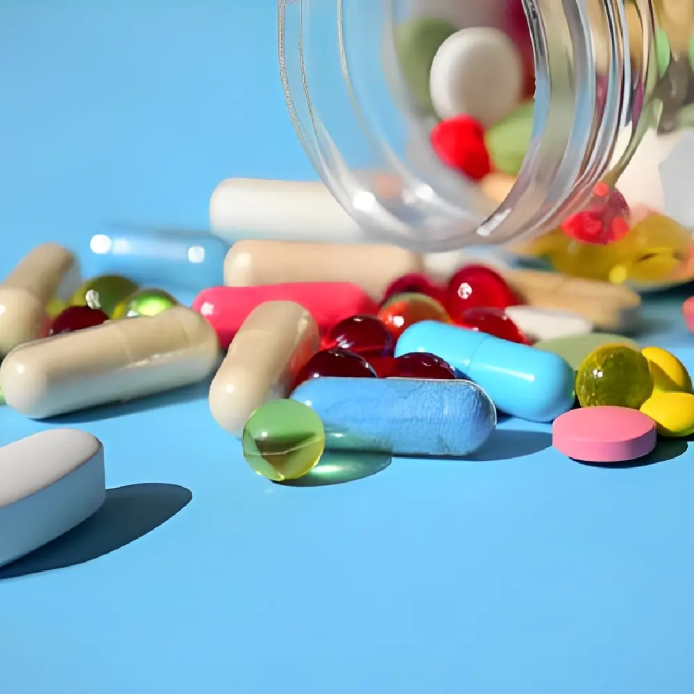 Variety of colorful pills and capsules spilling from a plastic bottle onto a blue surface.